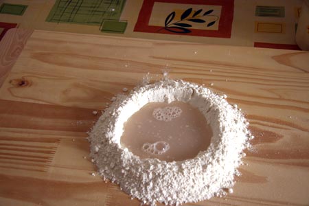 Step 2: Versate la farina a fontanella su una spianatoia e aggiungete al centro l’acqua tiepida e un pizzico di sale. Impastate per bene il tutto fino ad ottenere un composto omogeneo. Lasciatelo riposare ricoperto da un panno per 30 minuti.